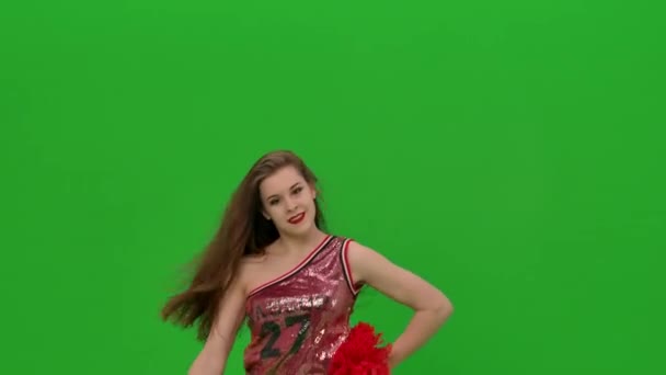 Mince pom-pom girl aux cheveux longs danse avec des pompons rouges. La jeune fille exécute une danse jubilatoire dans le studio sur un écran vert. Ferme là. Mouvement lent. — Video