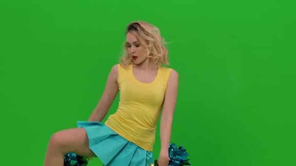 Une pom-pom girl danse une danse jubilatoire, s'accroupit gracieusement, fait des fentes verticales, agite ses cheveux. Une blonde en uniforme jaune-bleu s'entraîne en studio sur un écran vert. Ferme là. Mouvement lent. — Video