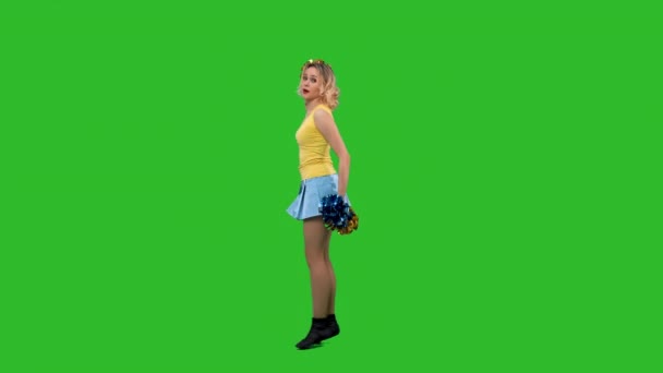 Чирлидерша танцует ликующий танец, кружится, грациозно приседает, делает вертикальный разрыв. Блондинка в жёлто-синей форме тренируется в студии на зелёном экране. Медленное движение. — стоковое видео