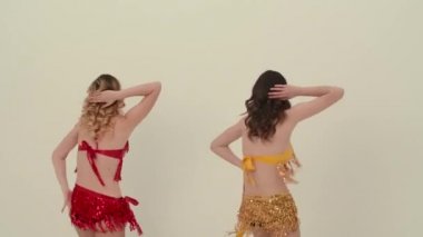 Kırmızı ve sarı üniformalı iki sevimli ponpon kız neşe içinde dans edip kalçalarını oynatıyorlar. Amigo kızlar yavaş çekimde beyaz bir stüdyoda senkronize dans ediyorlar. Kapat..