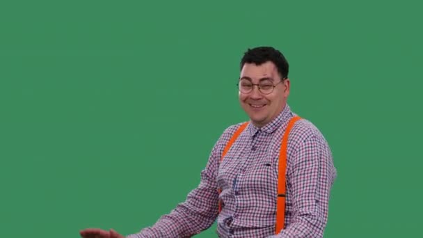 Человек со счастливым выражением лица танцует и разговаривает. Портрет мужчины в очках, в клетчатой рубашке с оранжевыми подтяжками в студии на зеленом экране. Медленное движение. Закрыть. — стоковое видео