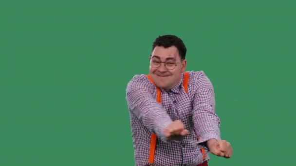 Задоволений чоловік танцює, танцюючи переможців. Портрет чоловіка в окулярах, в плетеній сорочці з помаранчевими підтяжками в студії на зеленому екрані. Повільний рух. крупним планом . — стокове відео