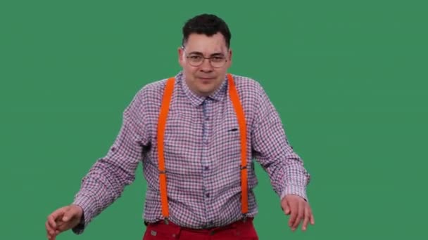 Ten muž tančí tanec robota. Portrét muže v brýlích, v kostkované košili s oranžovými podvazky ve studiu na zelené obrazovce. Zpomal. Zavřít. — Stock video
