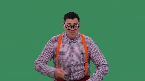 Mannen dansar, sjunger, jämnar ut ett ögonbryn, flirtar. Porträtt av en man i glasögon med tjocka linser, i rutig skjorta med orange hängslen i ateljén på en grön skärm. Sakta i backarna. Närbild. — Stockvideo