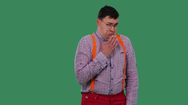 The unpleasantly shocked man covers his mouth with his hand and shows disgust. Portrait of a man in glasses, a plaid shirt with orange suspenders in the studio on a green screen. Slow motion. Close up — 비디오