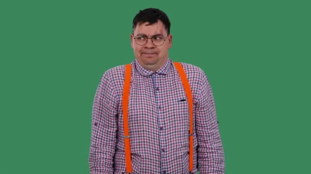 El hombre se encoge de hombros y sacude la cabeza. Retrato de un hombre en gafas, en una camisa a cuadros con tirantes anaranjados en el estudio en una pantalla verde. En cámara lenta. De cerca.. — Vídeo de stock
