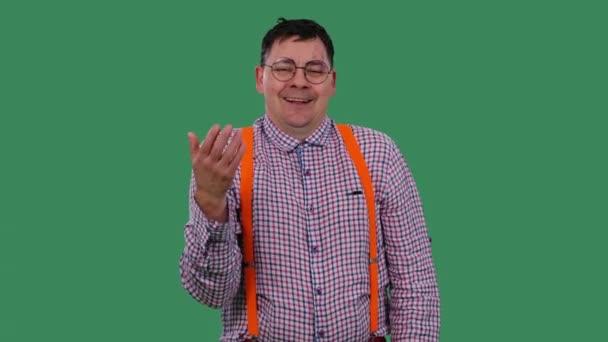 The man waves a hand at his face and exhales in relief. Portrait of a man in glasses, in a plaid shirt with orange suspenders in the studio on a green screen. Slow motion. Close up. — ストック動画