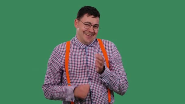 Un hombre sonriente se rasca la palma de la mano. Retrato de un hombre en gafas, en una camisa a cuadros con tirantes anaranjados en el estudio en una pantalla verde. En cámara lenta. De cerca.. — Vídeos de Stock