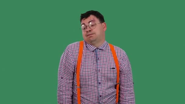 The tired, displeased man sighs heavily and shrugs. Portrait of a man in glasses, in a plaid shirt with orange suspenders in the studio on a green screen. Slow motion. Close up. — 비디오