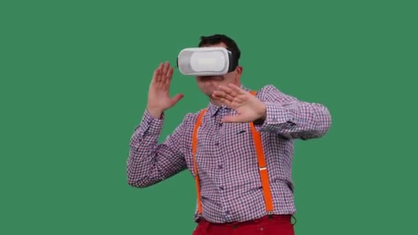 Ritratto di un uomo danzante con un auricolare di realtà virtuale o occhiali 3d sulla testa. Un uomo con gli occhiali, una camicia con le bretelle arancioni in studio su uno schermo verde. Al rallentatore. Da vicino.. — Video Stock