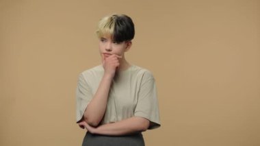 Moda modelinin portresi aklına bir fikir geldiği için mutlu ve düşünceli. Kısa saçlı, burnunda küpesi olan, kahverengi stüdyo arka planında poz veren şık bir kız. Kapatın. Yavaş çekim hazır 59.94fps