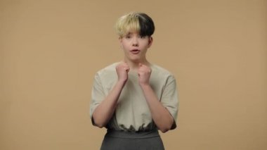 Moda modelinin portresi neşeyle kameraya bakıyor. Kısa saçlı, burnu küpeli, kahverengi stüdyo arka planında poz veren şık bir kız. Kapatın. Yavaş çekim hazır 59.94fps.