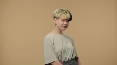 Moda modelinin portresi utanmadan kameraya bakıp gülümsüyor. Kısa saçlı, burnu küpeli, kahverengi stüdyo arka planında poz veren şık bir kız. Kapatın. Yavaş çekim hazır 59.94fps.