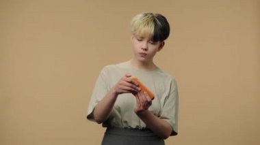Moda modelinin portresi akıllı telefondan oyun oynar ve zaferle neşelenir. Kısa saçlı, burnu küpeli, kahverengi stüdyo arka planında poz veren genç bir kız. Kapatın. Yavaş çekim hazır 59.94fps.