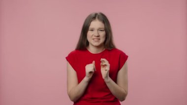 Moda modelinin portresi heyecanla kameraya bakıyor, sonra da zafer zaferini kutluyor. Kırmızı tişörtlü genç kız pembe stüdyo arka planında poz veriyor. Kapatın. Yavaş çekim hazır 59.94fps.
