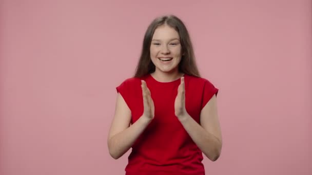 Porträtt av mode modell klappar händerna entusiastiskt och visar tummen upp. Ung flicka med långt hår i röd t-shirt poserar på rosa studio bakgrund. Närbild. Slow motion klar 59,94fps. — Stockvideo