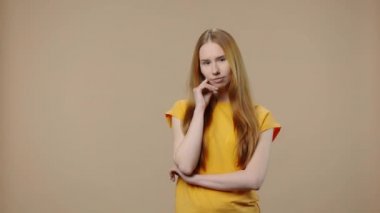 Doğal güzelliği olan bir modelin portresi baştan çıkarıcı bir gülümsemeyle işaret parmağını sallayarak tehdit eder. Uzun saçlı genç kız kahverengi stüdyo arka planında poz veriyor. Kapatın. Yavaş çekim hazır 59.94fps.