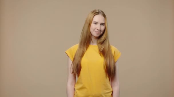 Porträt eines Models mit natürlicher Schönheit, das kokett in die Kamera schaut und lächelt. Junges Mädchen mit langen Haaren in gelbem T-Shirt posiert auf braunem Studiohintergrund. Aus nächster Nähe. Zeitlupe bereit 59.94fps. — Stockvideo