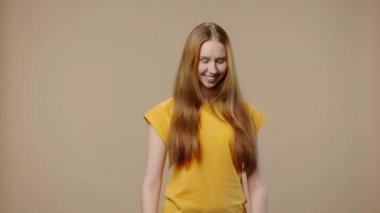 Doğal güzelliği olan bir modelin portresi. Gülümseyen, parmaklarıyla kalbini gösteren ve sonra öpüşen. Uzun saçlı genç kız kahverengi stüdyo arka planında poz veriyor. Kapatın. Yavaş çekim hazır 59.94fps.