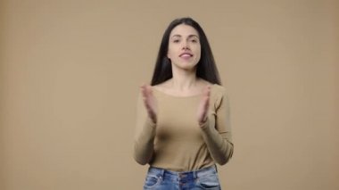 Doğal güzelliğe sahip bir modelin portresi ellerini alkış tutarak mutluluk ve keyif veriyor. Uzun saçlı esmer kız kahverengi stüdyo arka planında poz veriyor. Kapatın. Yavaş çekim hazır 59.94fps.