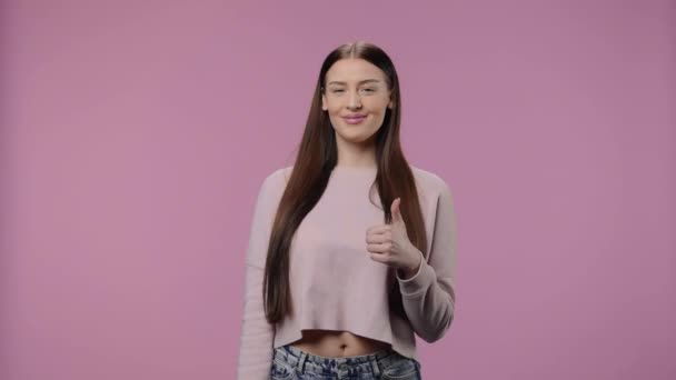 Retrato de una modelo de belleza mostrando los pulgares hacia arriba, gesto como y sonriendo. Chica joven con el pelo largo posa sobre fondo púrpura estudio. De cerca. Cámara lenta lista 59.94fps. — Vídeo de stock