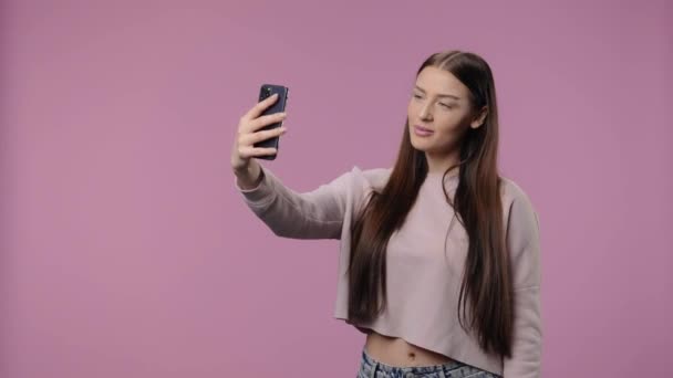Portret van een schoonheidsmodel dat selfie maakt op mobiele telefoon en dan foto 's maakt. Jong meisje met lang haar poseert op paarse studio achtergrond. Sluit maar af. Slow motion klaar 59,94fps. — Stockvideo