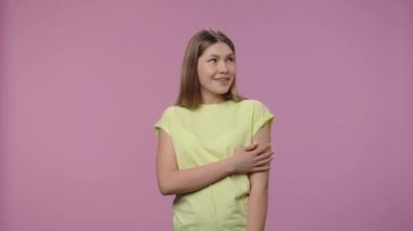 Doğal güzellikte bir modelin portresi güzel bir şeyin hayalini kuruyor ve gülümsüyor. Sarı tişörtlü, uzun saçlı genç kız mor stüdyo arka planında poz veriyor. Kapatın. Yavaş çekim hazır 59.94fps
