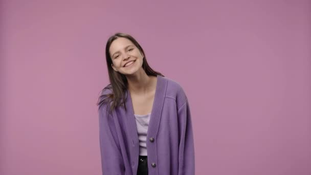 Retrato de una modelo con belleza natural mirando coqueta a la cámara y sonriendo. Chica joven con el pelo largo posa sobre fondo púrpura estudio. De cerca. Cámara lenta lista 59.94fps. — Vídeo de stock