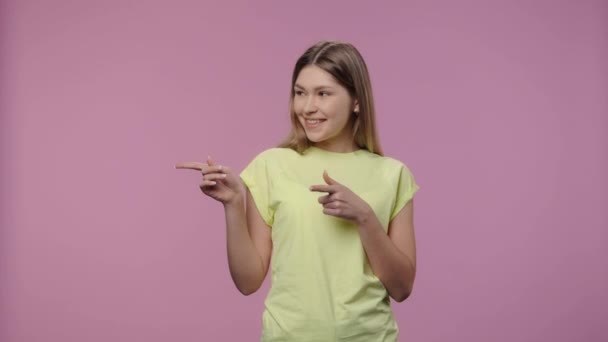 Retrato de modelo con belleza natural apuntando lado de la mano para algo, luego muestra el pulgar como. Chica joven en camiseta amarilla posa sobre fondo púrpura estudio. De cerca. Cámara lenta lista 59.94fps. — Vídeo de stock