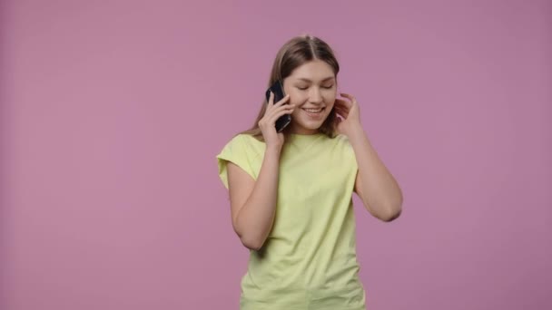 Retrato de um modelo com beleza natural falando para celular e se alegrar. Menina com cabelos longos em amarelo t-shirt poses no fundo do estúdio roxo. Fecha. Movimento lento pronto 59.94fps. — Vídeo de Stock