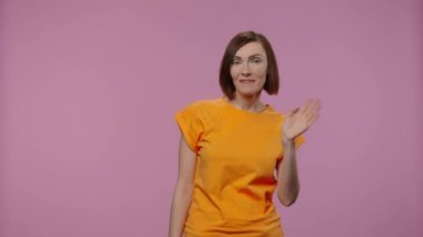 Çekici modelin portresi el sallıyor. Sarı tişörtlü kısa saçlı genç kadın mor stüdyo arka planında poz veriyor. Kapatın. Yavaş çekim hazır 59.94fps.