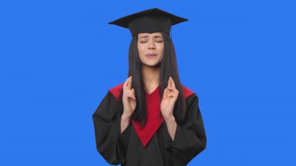 Portrait of female student in graduation costume looking with excitement, then celebrating her victory triumph. Young woman posing on blue screen background. Close up. Slow motion ready 59.94fps. — Stock Video