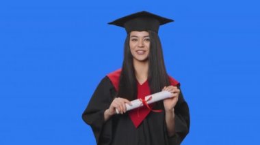 Mezuniyet kostümü giymiş kadın öğrenci portresi, elinde diploma ve ilginç bilgiler var. Stüdyoda poz veren genç bir kadın. Kapatın. Yavaş çekim hazır 59.94fps.