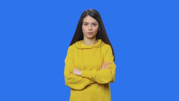 Portrait de brune concentré penser à quelque chose, aucune idée. Jeune femme aux cheveux longs en sweat-shirt jaune posant en studio avec fond bleu. Ferme là. Ralenti prêt 59.94fps. — Video