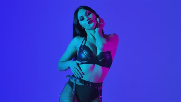 Sexy brunette dalam pakaian kulit hitam menari erotis di studio gelap diterangi oleh lampu biru. Sensual penari telanjang, tari pribadi, pergi pergi. Tutup. Gerakan lambat. — Stok Video