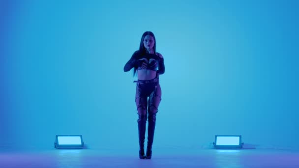 Sexy brunette in zwart lederen lingerie danst erotisch in een donkere studio verlicht door blauwe lichten. Sensuele stripper dans, privé dans, ga. Langzame beweging. — Stockvideo