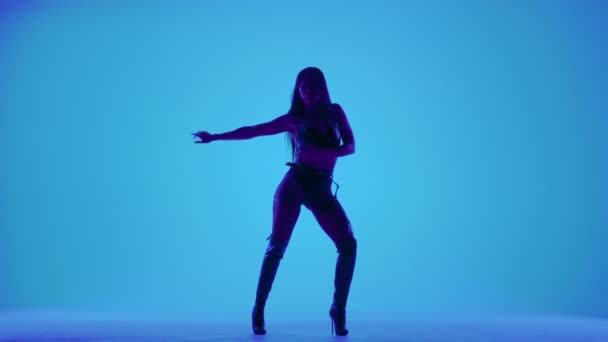 Sexy morena en lencería de cuero negro está bailando eróticamente en un estudio oscuro iluminado por luces azules. Baile de stripper sensual, baile privado, vamos. Silueta. Movimiento lento. — Vídeos de Stock