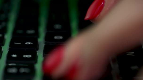 Девушка печатает текст на клавиатуре ноутбука, работает. Закрываем девочки клавиатуру, пальцы в зеленом неоновом свете. Движение камеры по клавиатуре, некоторые клавиши размыты. Медленное движение. — стоковое видео