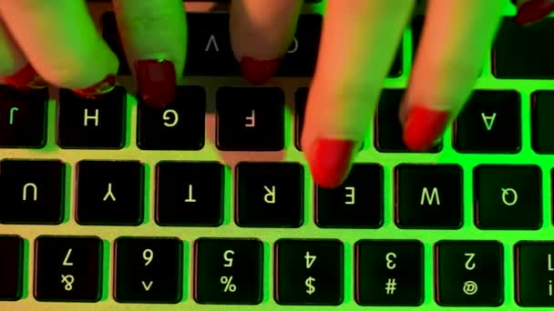 Top view of the hands of a girl with a red manicure, typing on a laptop, writing emails, browsing the Internet. Female hands working on a computer in green neon light. Slow motion. Close up. — Stock Video