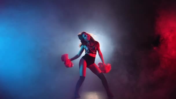 Ung cheerleader med pompoms i uniform dansar på svart rökig studio bakgrund med rött och blått ljus. Silhuett av vackra dansare utför jublande dans. Slow motion klar 59,94fps. — Stockvideo