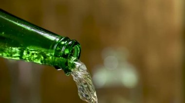 Yeşil, sisli bir şişeden taze, soğuk bira akıntısı. Bulanık sarı arka plana sıçramış ve farklı yönlere sıçramış. Bira fıskiyesi. Kapatın. Yavaş çekim.