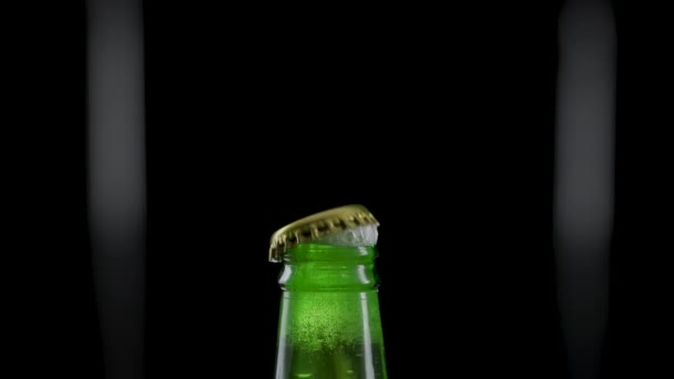 Macro shot of cap popping out of green glass bottle and explosion of splash carbonated beer. Amber liquid under pressure bursts out of bottle and fountains up. Black background. Close up. Slow motion. — Wideo stockowe