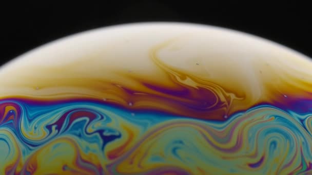 A macro shot of the surface of thin film of soap with rainbow colors creating a beautiful swirling effect. Semicircle of a soap bubble with colored streaks on a black background. Close up. Slow motion — Stockvideo