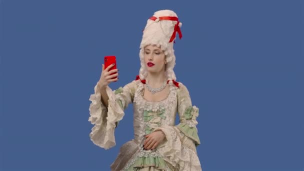 Πορτρέτο της courtier κυρία σε λευκό vintage φόρεμα δαντέλα και περούκα κάνοντας selfie στο κινητό τηλέφωνο. Νεαρή γυναίκα ποζάρει στο στούντιο με φόντο την μπλε οθόνη. Κλείσε. Αργή κίνηση έτοιμη 59.94fps. — Αρχείο Βίντεο