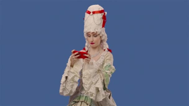 Ritratto di signora cortigiano in abito bianco vintage pizzo e parrucca gioca gioco su smartphone e vince. Giovane donna in posa in studio con sfondo schermo blu. Chiudete. Movimento lento pronto 59.94fps. — Video Stock