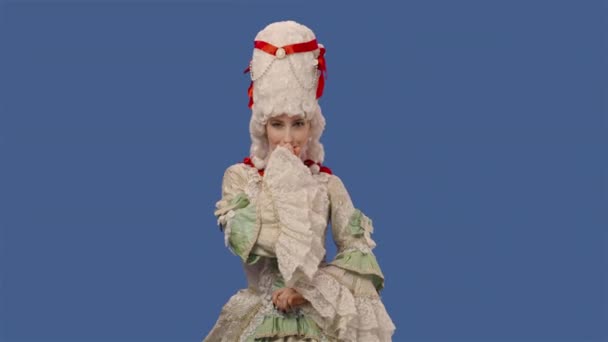 Portrait of courtier lady in white vintage dress and wig smiling coquettishly, making eyes, winking. Young woman posing in studio with blue screen background. Close up. Slow motion ready 59.94fps. — стоковое видео