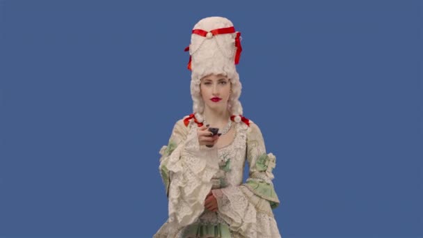 Portrait of courtier lady in white vintage dress and wig watching TV and changing channels using remote. Young woman posing in studio with blue screen background. Close up. Slow motion ready 59.94fps. — стоковое видео