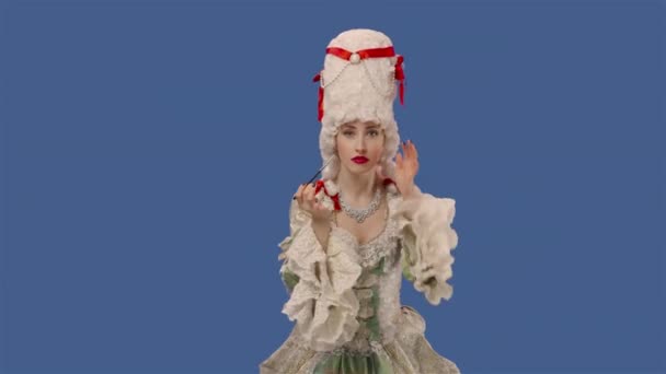 Portrait de courtisane en dentelle blanche vintage robe et perruque se maquille avec un pinceau. Jeune femme posant en studio avec fond bleu. Ferme là. Ralenti prêt 59.94fps. — Video