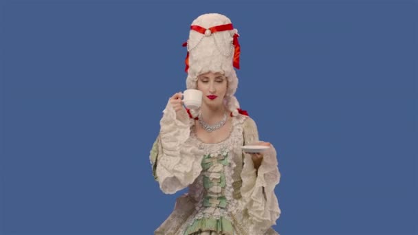 Porträt einer Hofdame in weißem Spitzenkleid und Perücke, die Kaffee aus einer Tasse trinkt. Junge Frau posiert im Studio mit blauem Hintergrund. Aus nächster Nähe. Zeitlupe bereit 59.94fps.