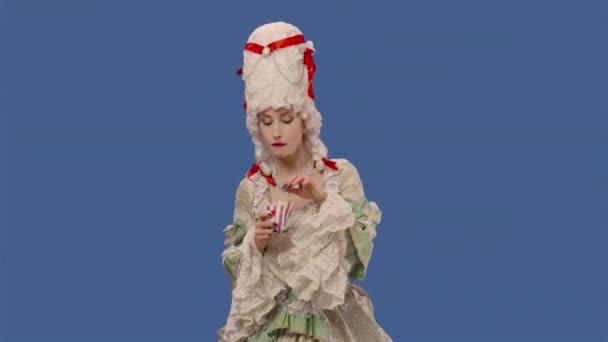 Portrait de courtisane en dentelle vintage blanche et perruque, savourant de délicieuses frites. Jeune femme posant en studio avec fond bleu. Ferme là. Ralenti prêt 59.94fps. — Video